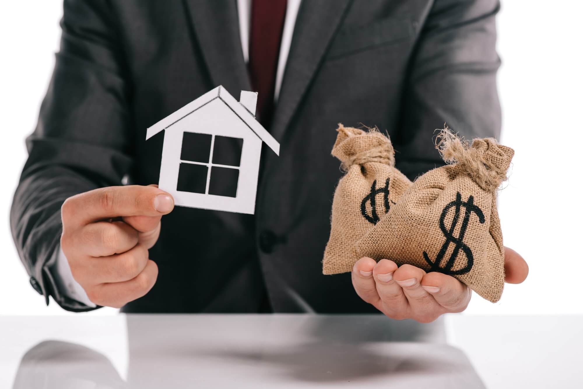 Cropped view of mortgage broker holding paper house and moneybags isolated on white