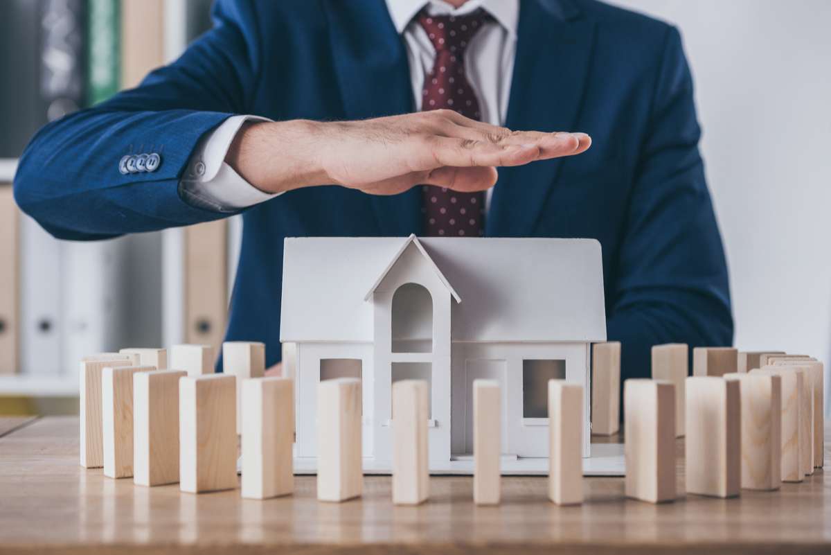 Cropped view of risk manager covering house model surrounded with wooden blocks with hand (R) (S)