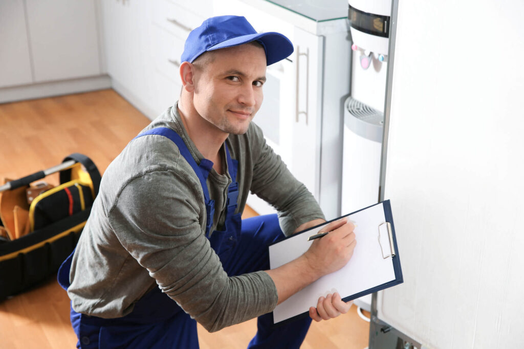 Male technician with clipboard examining broken refrigerator in kitchen